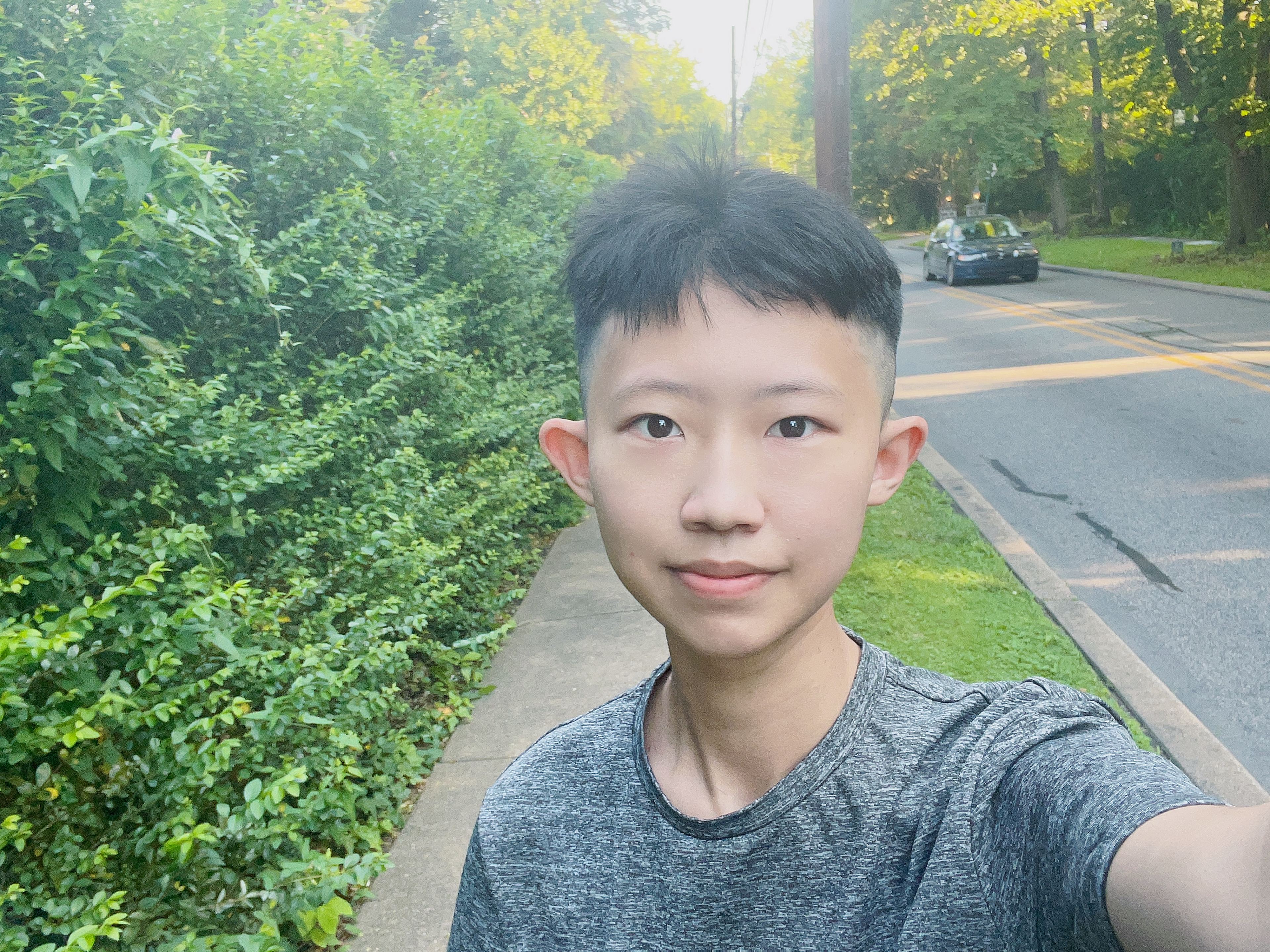 photograph of Vic Wen standing on a sidewalk with tall green shrubs